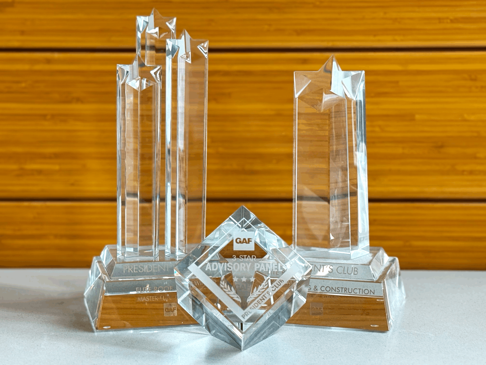 Crystal GAF awards presented to Elite Roof and Solar, including the 2025 3-Star President’s Club Award and 3-Star Advisory Panel recognition, displayed on a white countertop with a wooden background. These prestigious honors highlight Elite Roof and Solar’s excellence in roofing and solar services across North Carolina and the Carolinas.