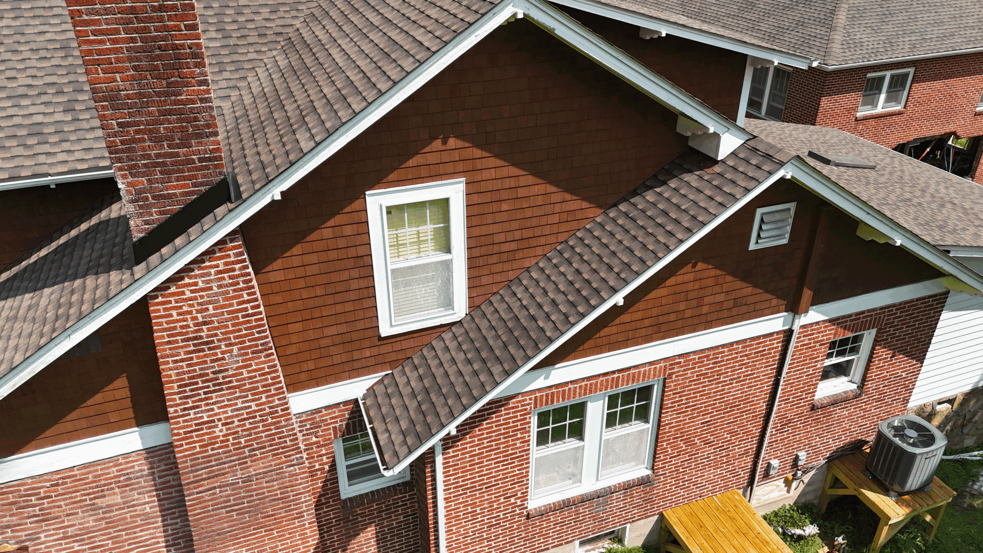 Aerial view of a brick home with newly installed asphalt shingles and seamless white gutters along the roofline.